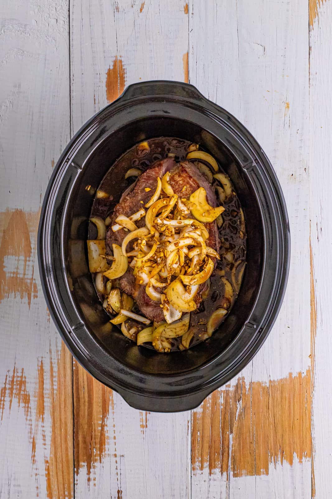 pot roast added to oval slow cooker with onions added on top. 