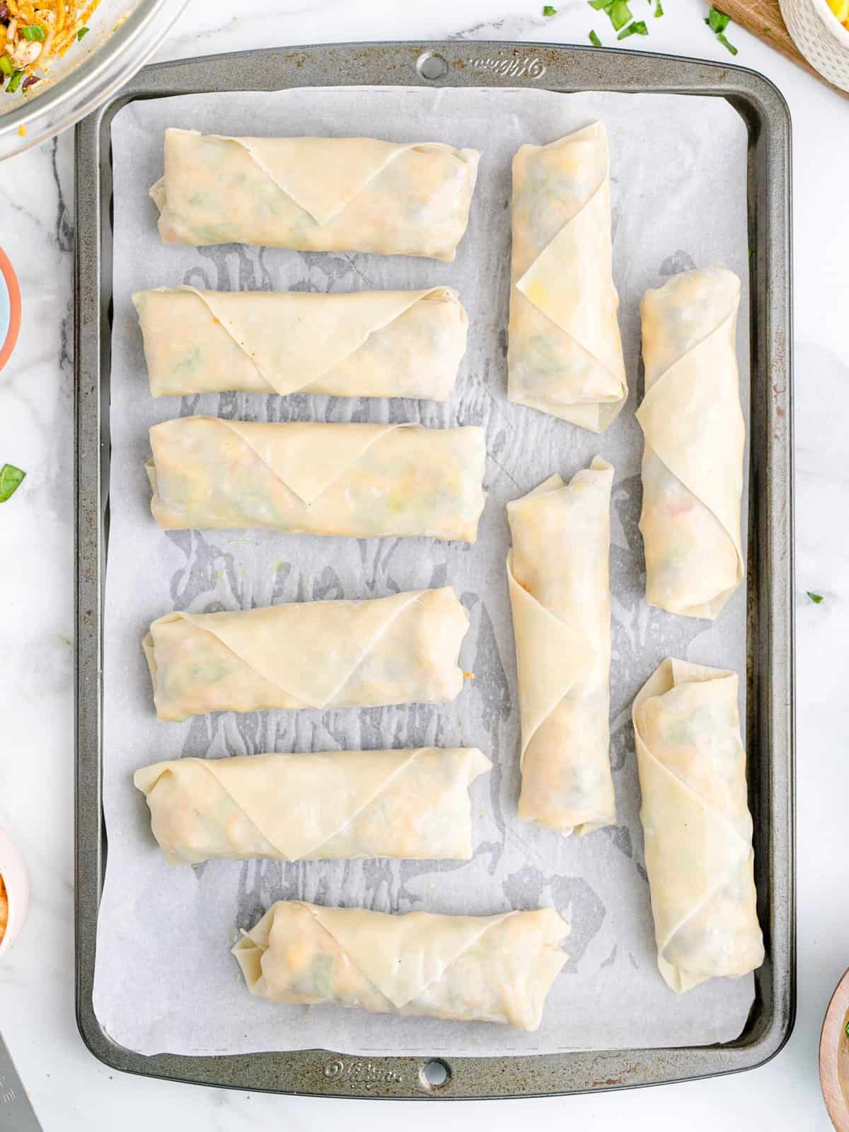 Multiple egg rolls on a parchment lined baking tray.
