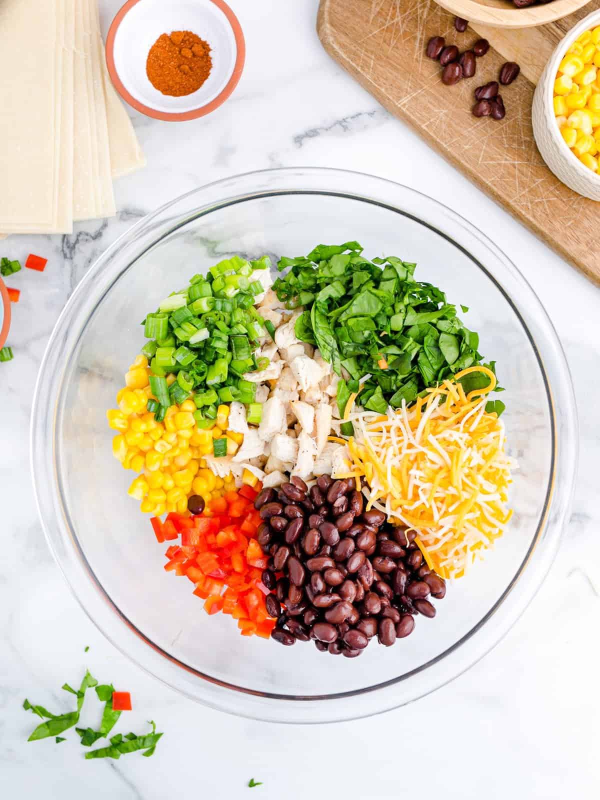 Chicken, corn, red bell pepper, sliced green onions, black beans, chopped spinach, Mexican blend cheese in a glass bowl.