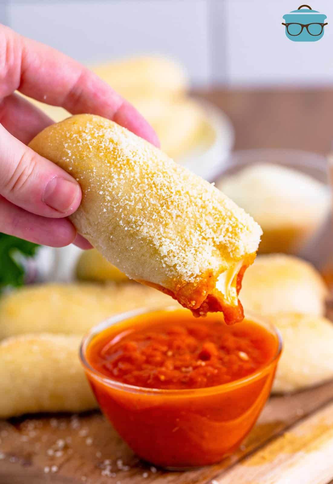 Fingers holding a Bosco stick after it was dipped in marinara sauce.