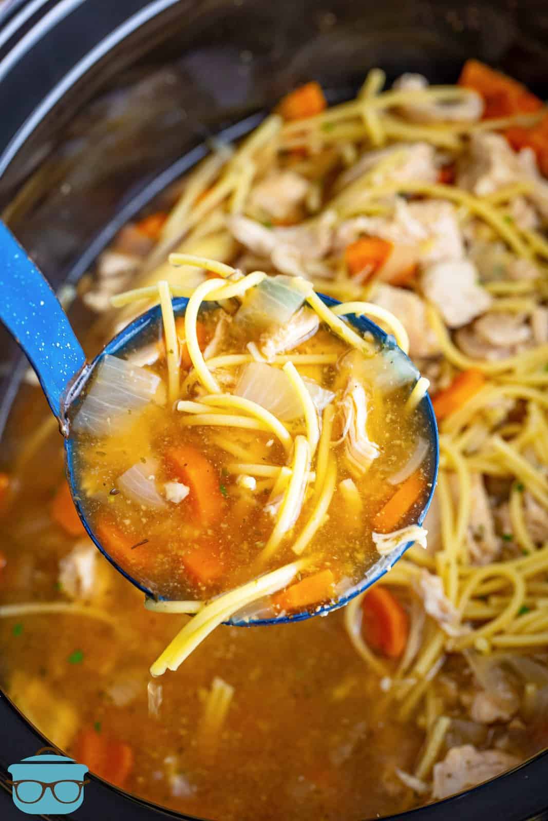 A ladle holding Chicken Noodle Soup overtop of the Slow Cooker.
