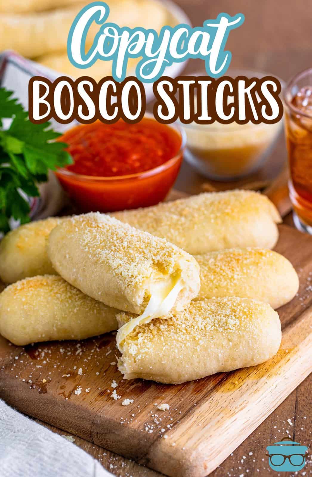 A few Bosco sticks with a broken open one resting on top on a wooden board with a small bowl of marinara sauce in the background.
