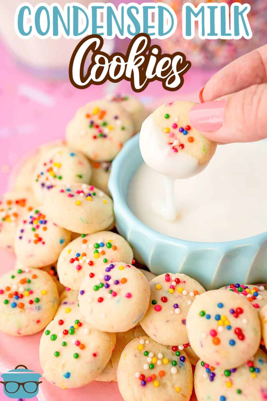 A hand dipping a cookie in a blue bowl of frosting.