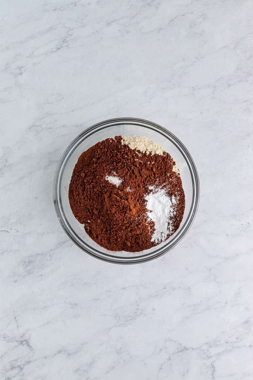 A small glass mixing bowl of flour, cocoa powder, baking powder.