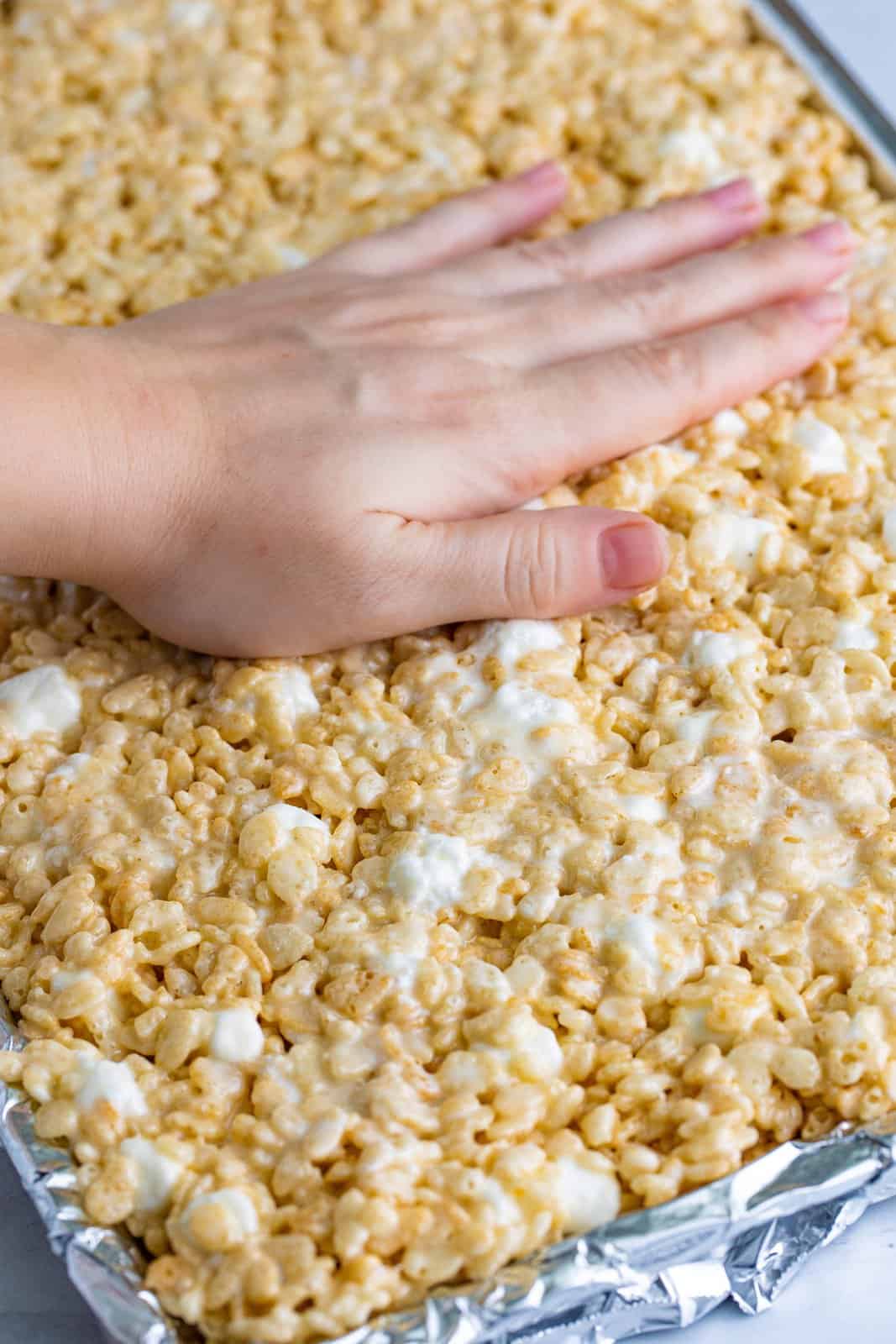 A hand pressing down on rice krispie treats in a pan.