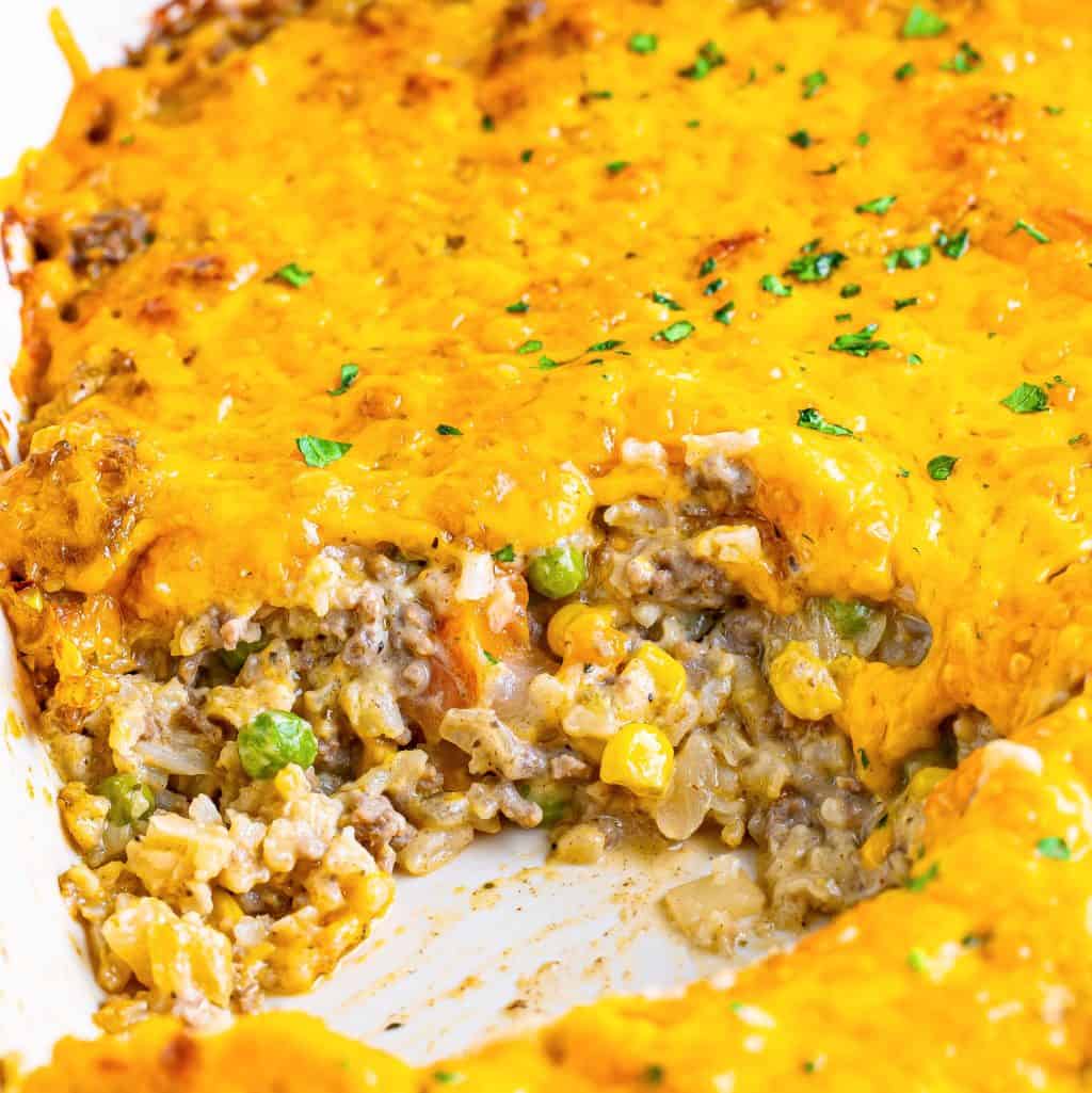 Close up of a homemade cheesy ground beef and rice casserole with a serving missing.