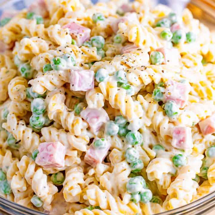 A close up of pasta salad with ham and peas.