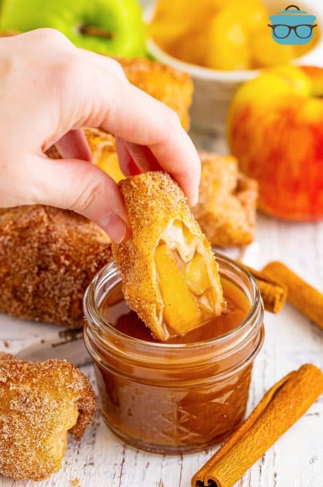 An apple pie egg roll being dipped in a sweet caramel sauce.