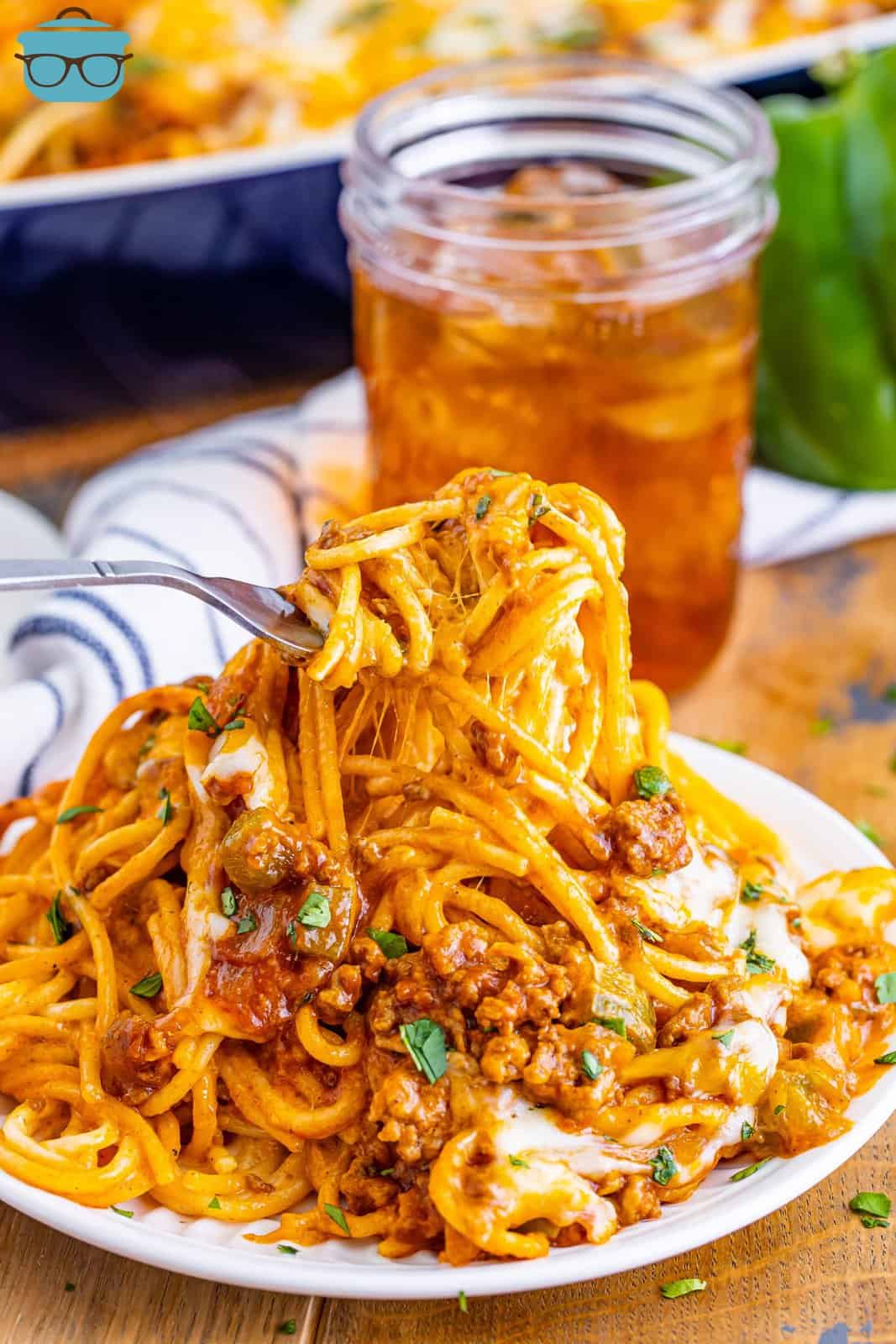 A fork holding a bite of Mexican million dollar spaghetti over a plate of spaghetti.