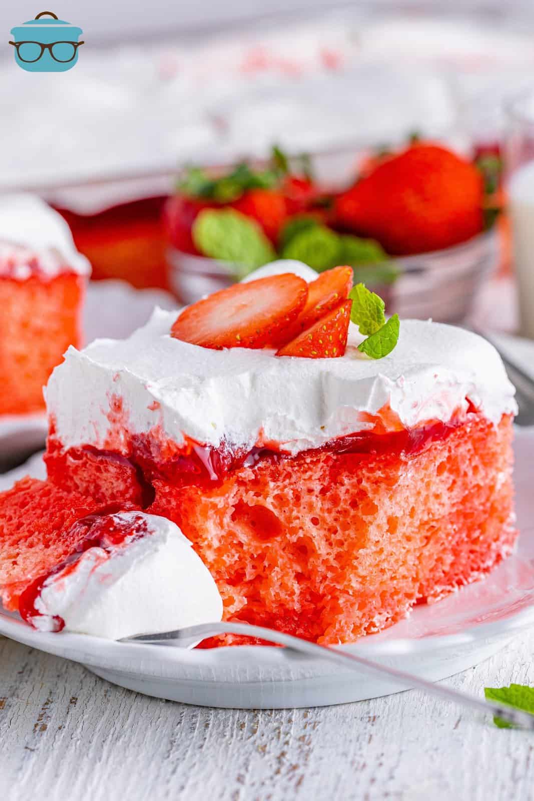 A plate with a serving of Strawberry Poke cake and a fork in front with a bite of it.