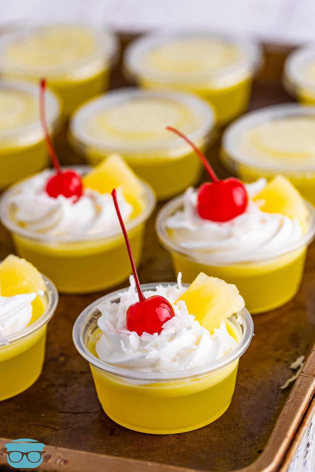 A few Pina Colada Jell-O shots with whipped cream, cherries, and a pineapple bit on top.