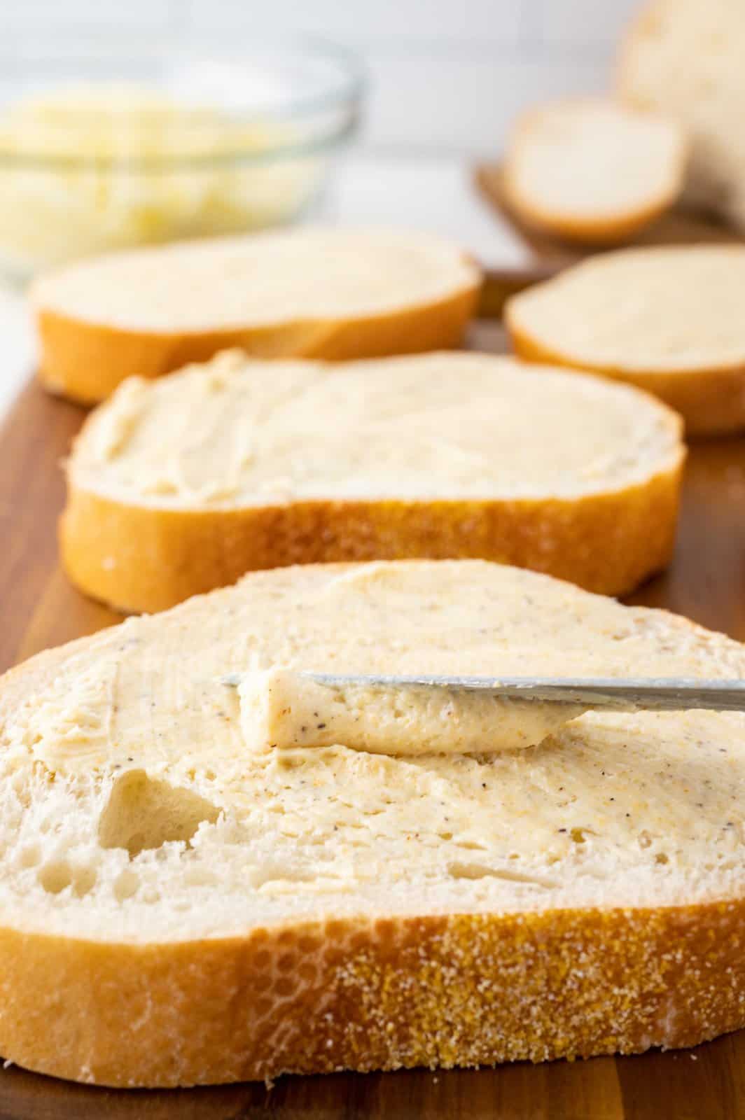 A knife spreading garlic butter on a slice of bread. 