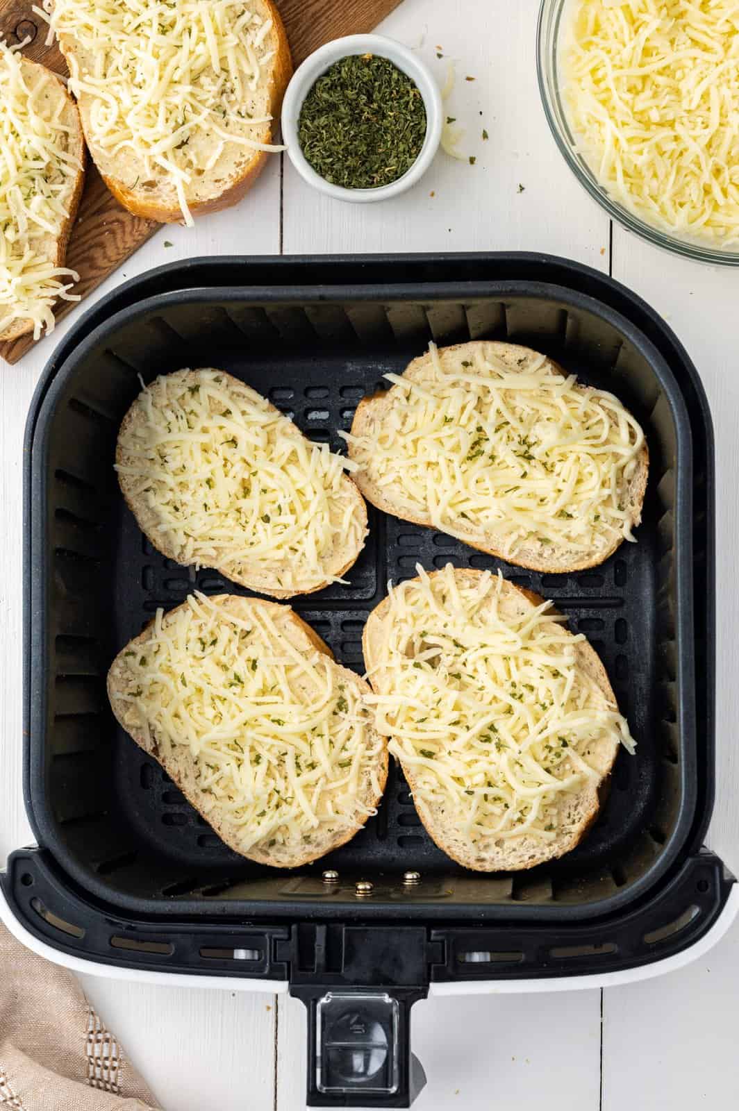 An Air Fryer basket with 4 pieces of garlic bread topped with cheese.