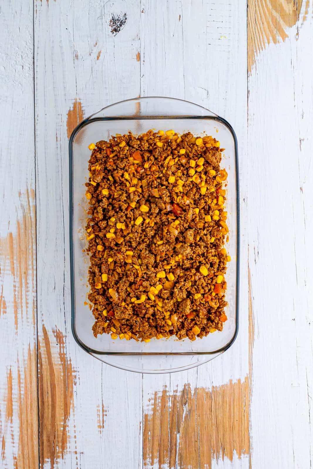 A baking dish with cooked ground beef, onion, taco seasoning, salsa, and corn.