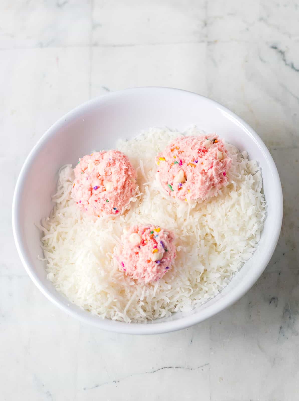 A bowl of sweetened coconut with 3 balls of cake mix dip.