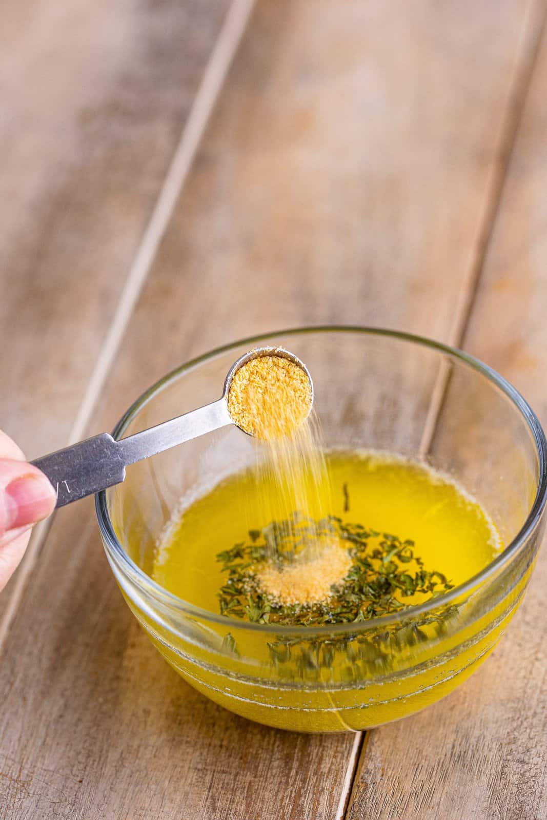 A small mixing bowl with melted butter, parsley flakes, and garlic powder being poured in.