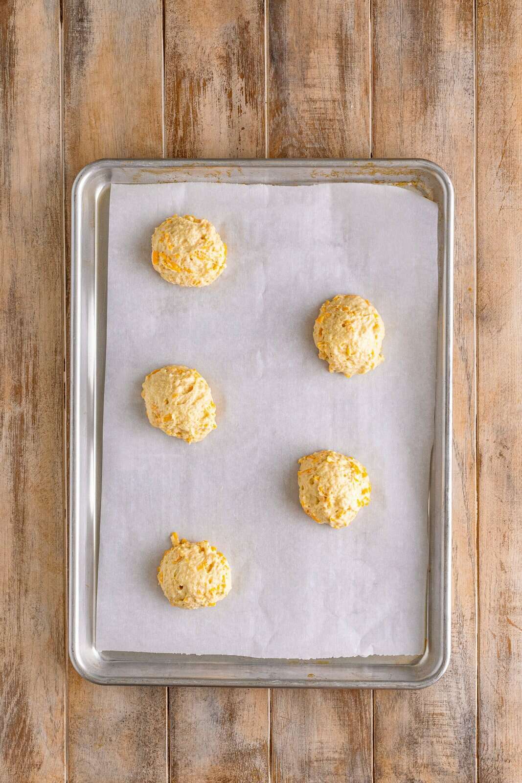The parchment lined baking sheet with cheddar biscuit tables.