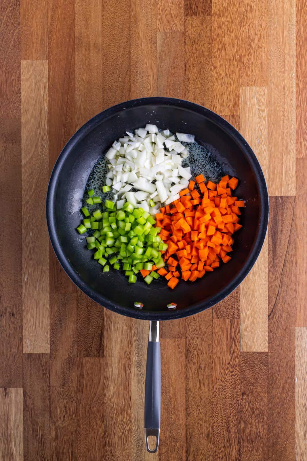 A skillet with onion, carrots and celery in it. 