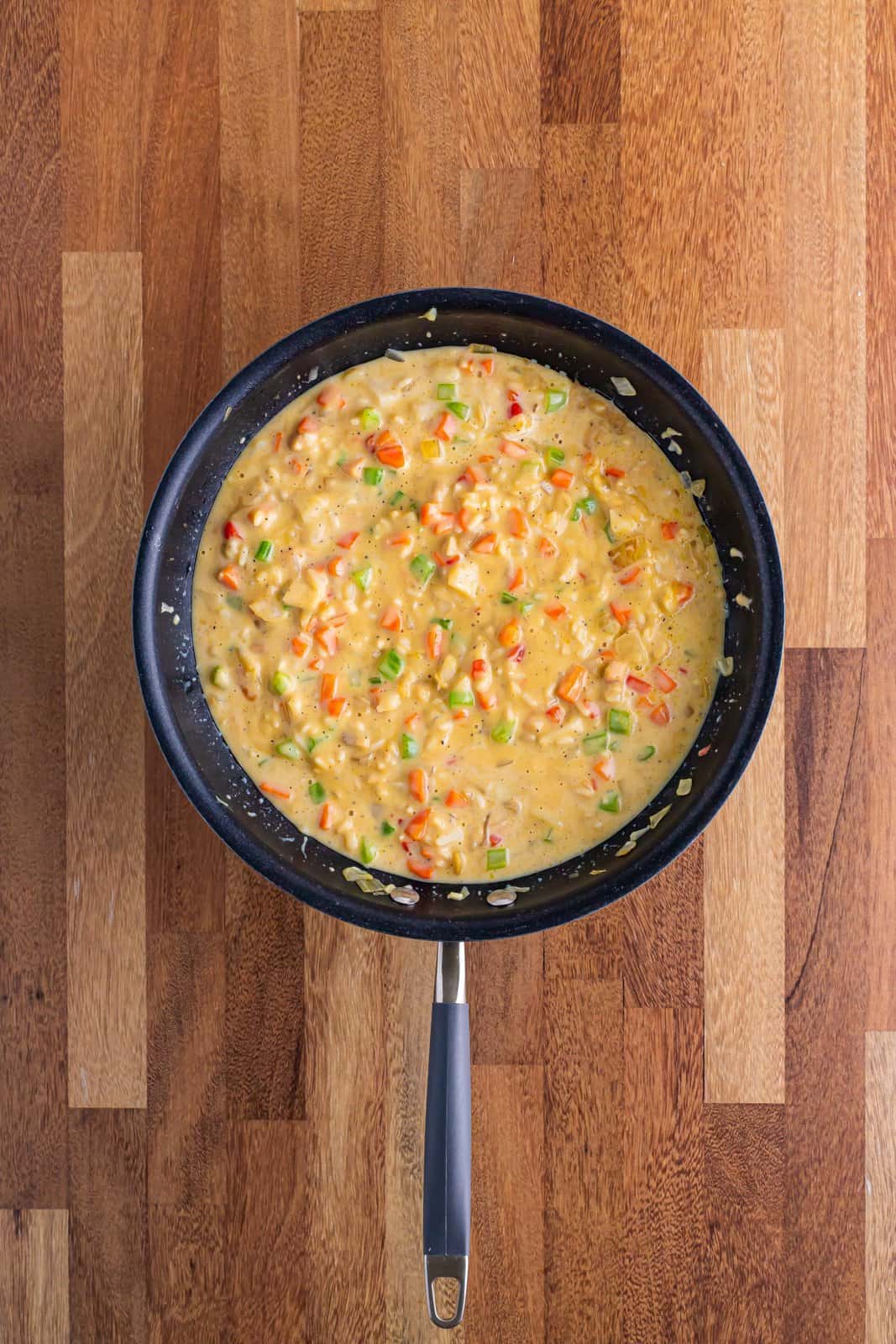 A skillet with carrots, celery, onion, butter, water chestnuts, cream of chicken soup, chicken and rice soup, milk, pepper and soy sauce.