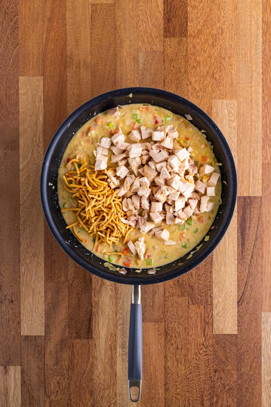 A skillet with ingredients cooking down and chicken and some chow mein noodles on top. 