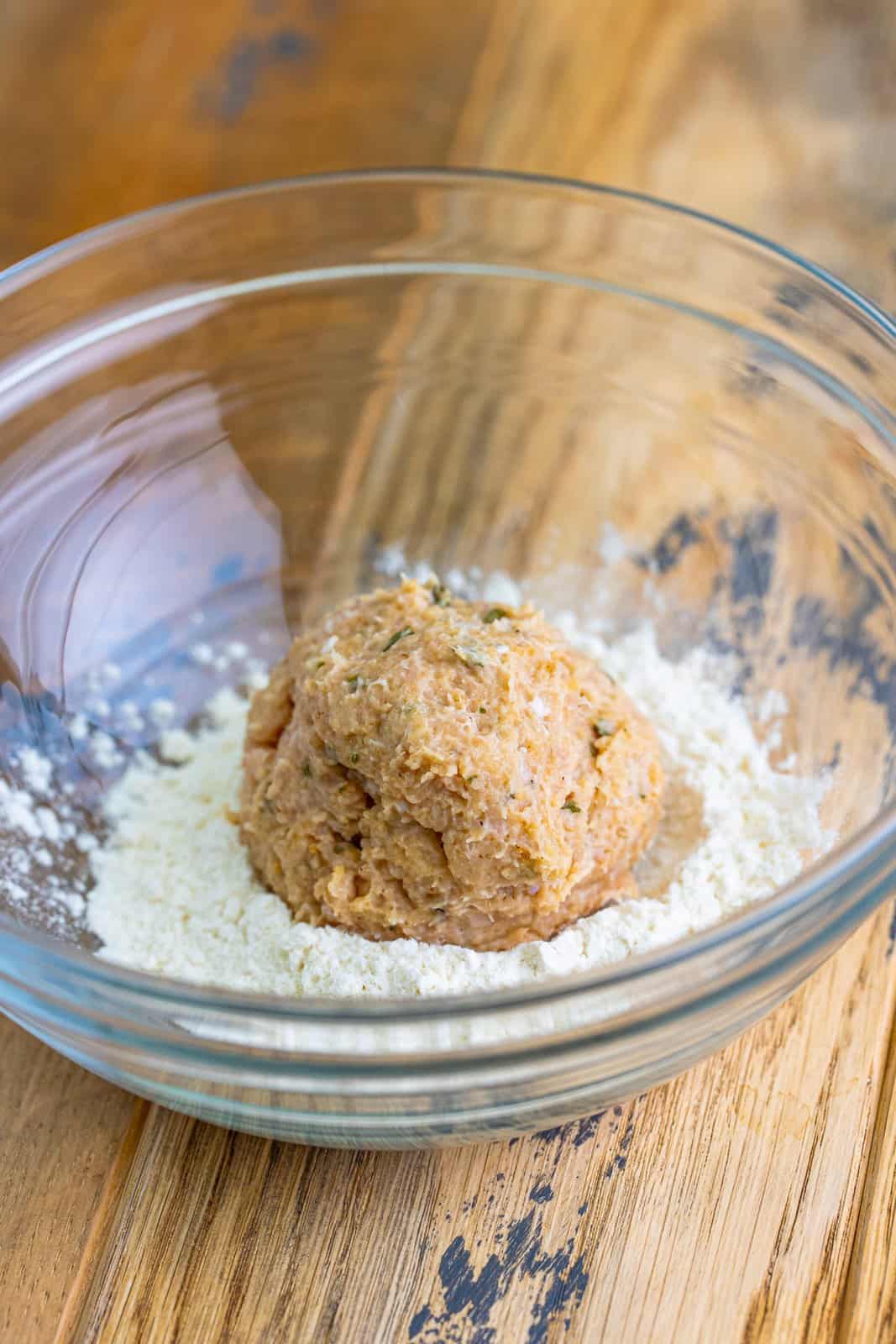 Ground chicken and spices in a ball in a bowl of flour.