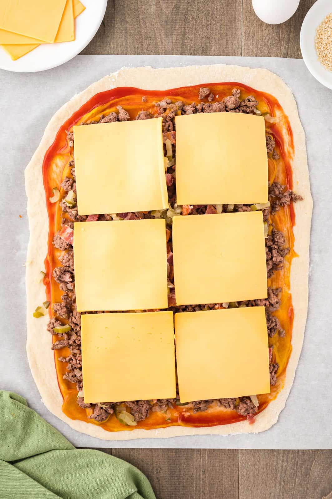 American cheese slices layered overtop of a ground beef mixture on bread dough.