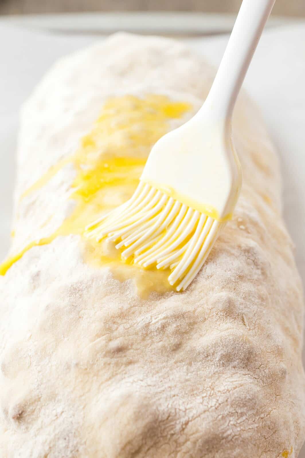 A pastry brush brushing a beaten egg on a rolled up loaf of bread. 