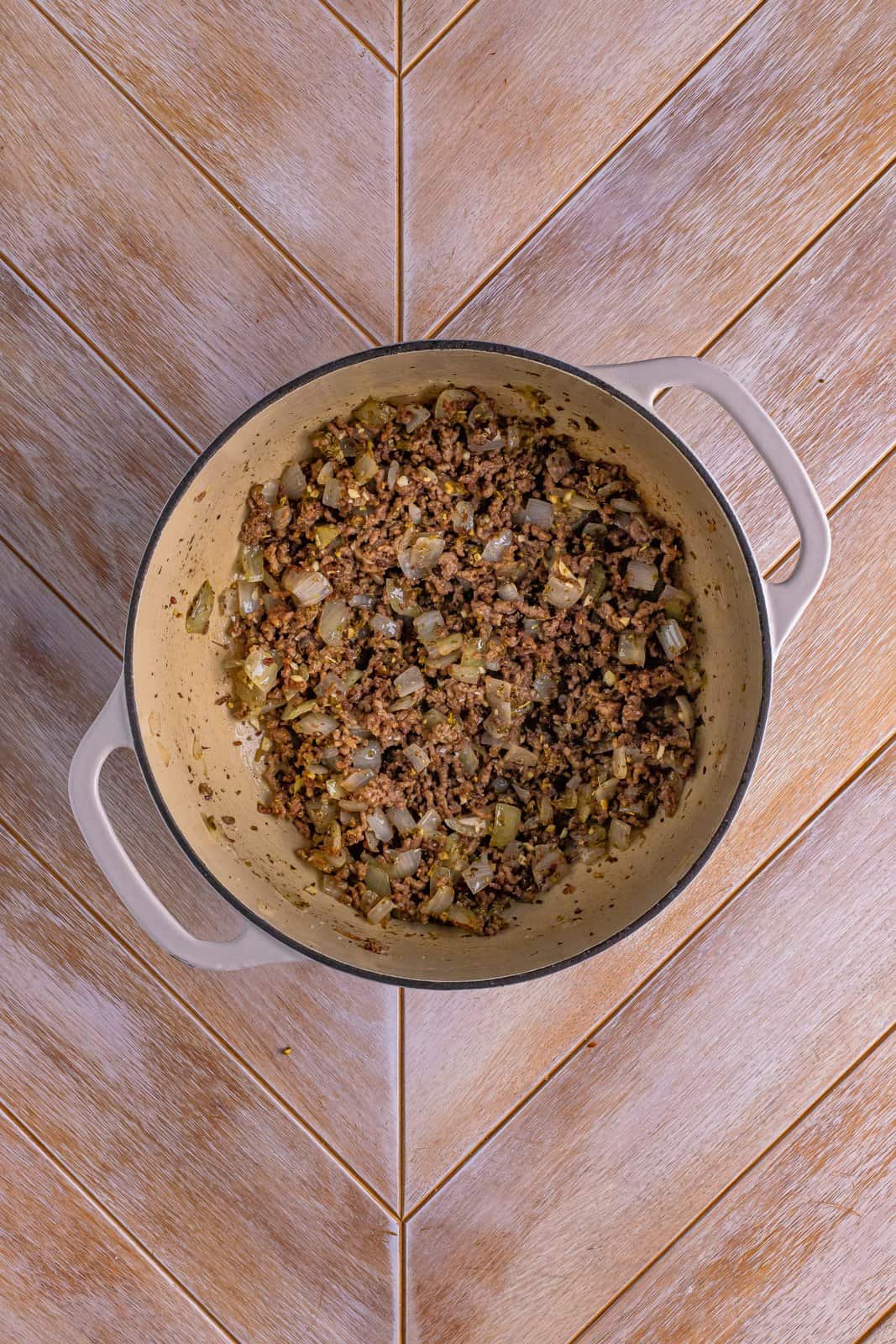 Dutch oven with cooked ground beef, diced onion, and spices mixed in.