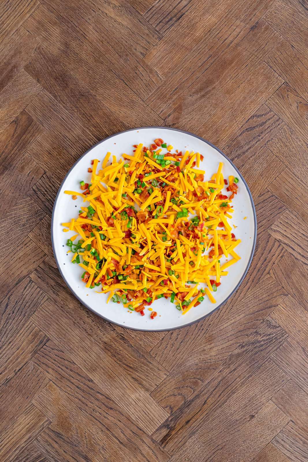 A plate of chives, shredded cheese, and crumbled bacon.