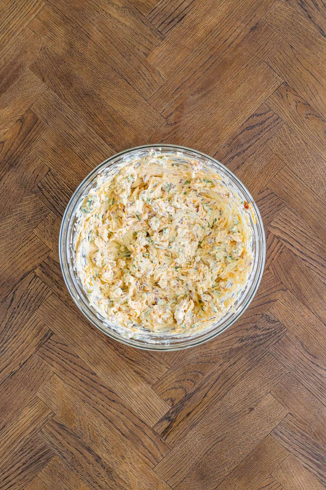 A glass mixing bowl of cream cheese, ranch seasonings, and other spices.