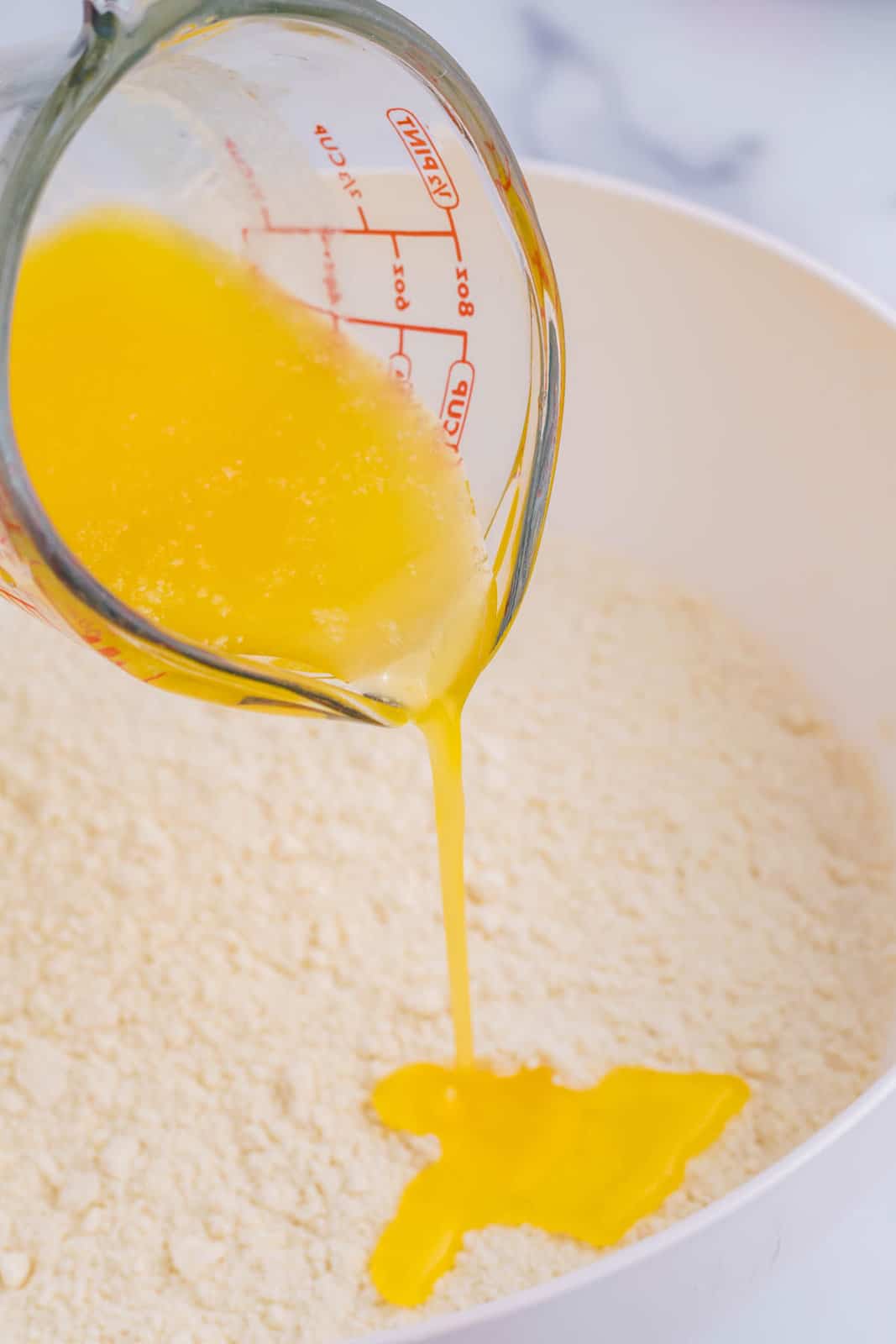 A measuring cup pouring melted butter in a mixing bowl of cake mix and lemon extract.