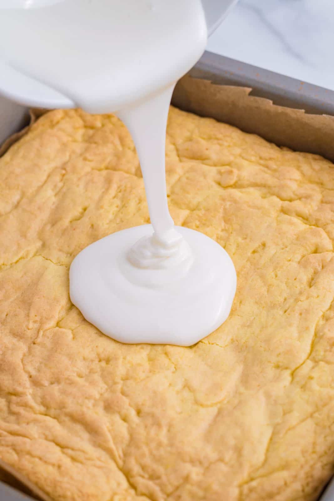 White glaze being poured on Lemon Brownies.