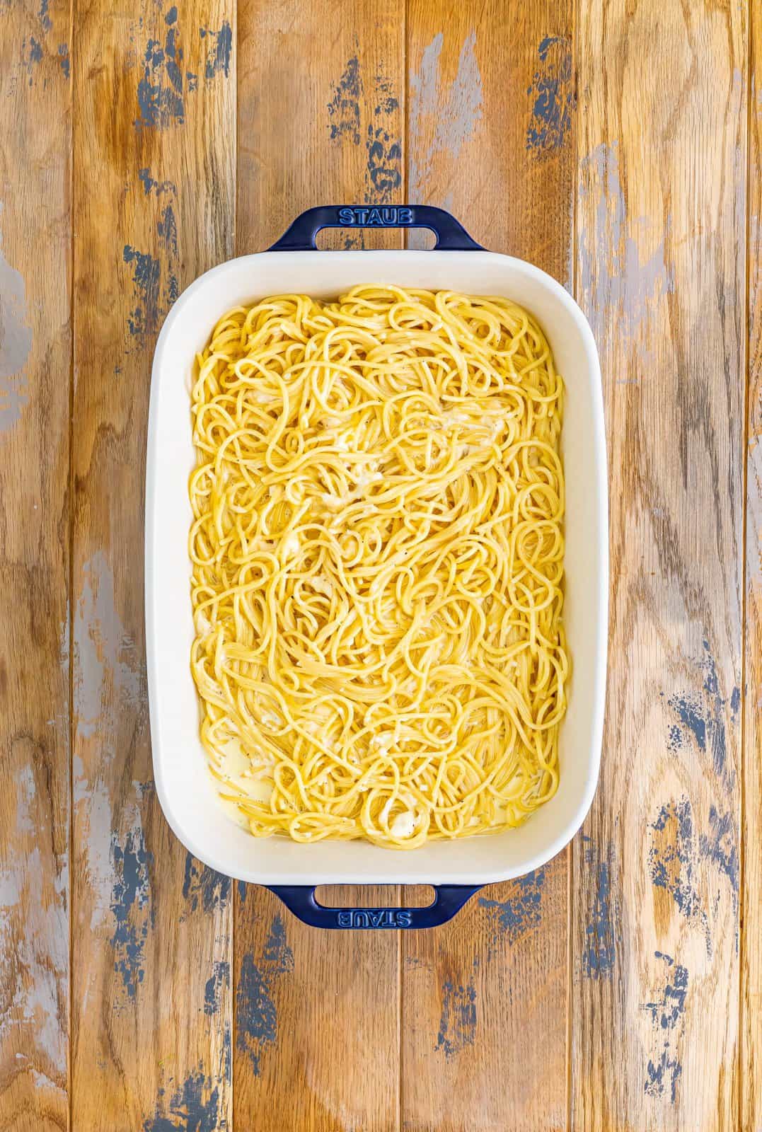 A baking dish with cooked spaghetti in a cream butter sauce.