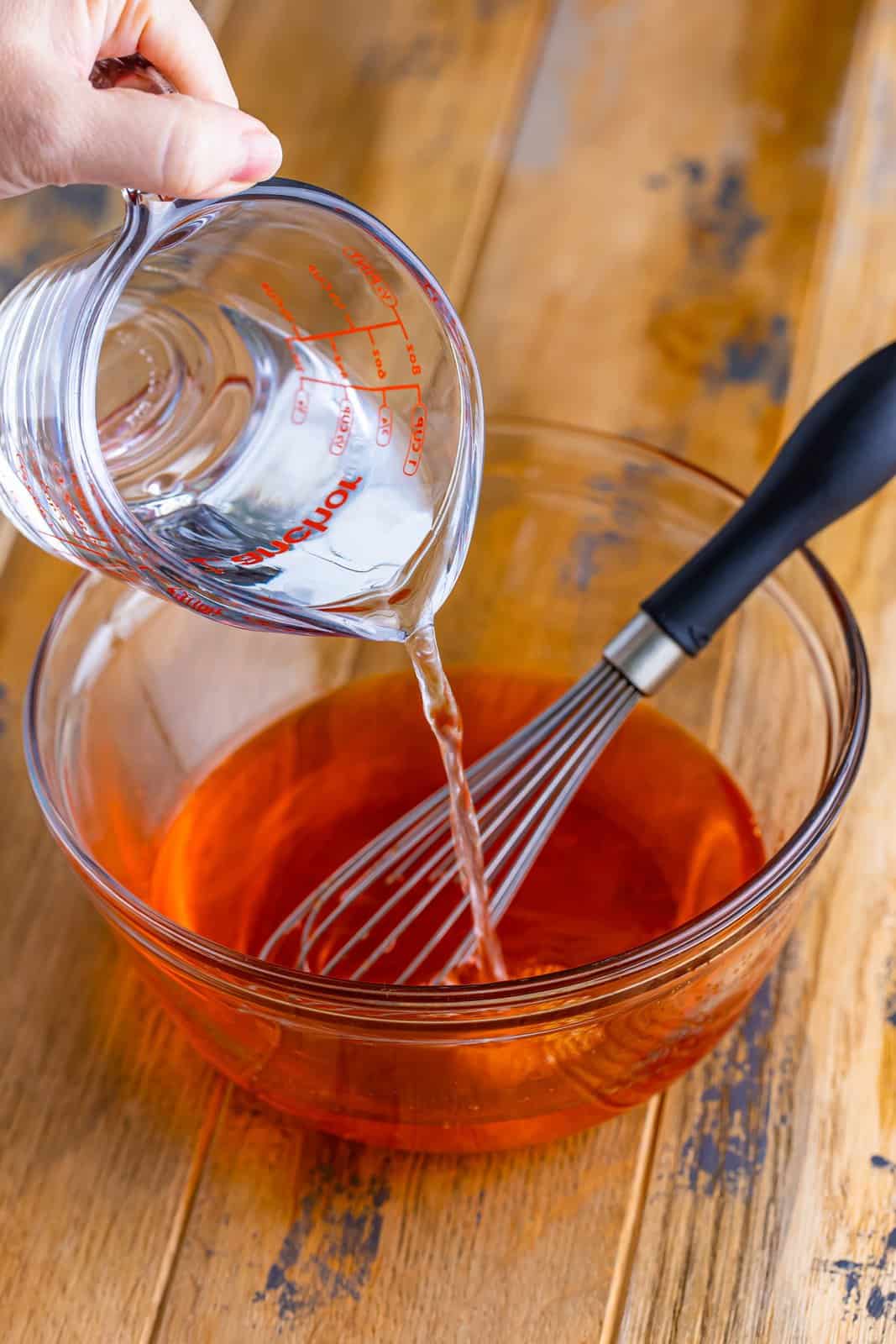 Water being poured into a mixing bowl of Orange Jello powder. 