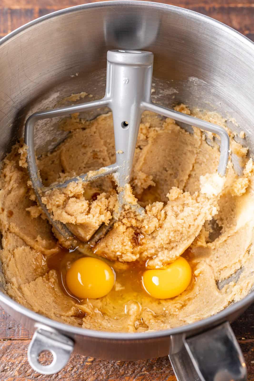 Vanilla extract, and eggs being mixed with brown sugar, sugar, and butter. 