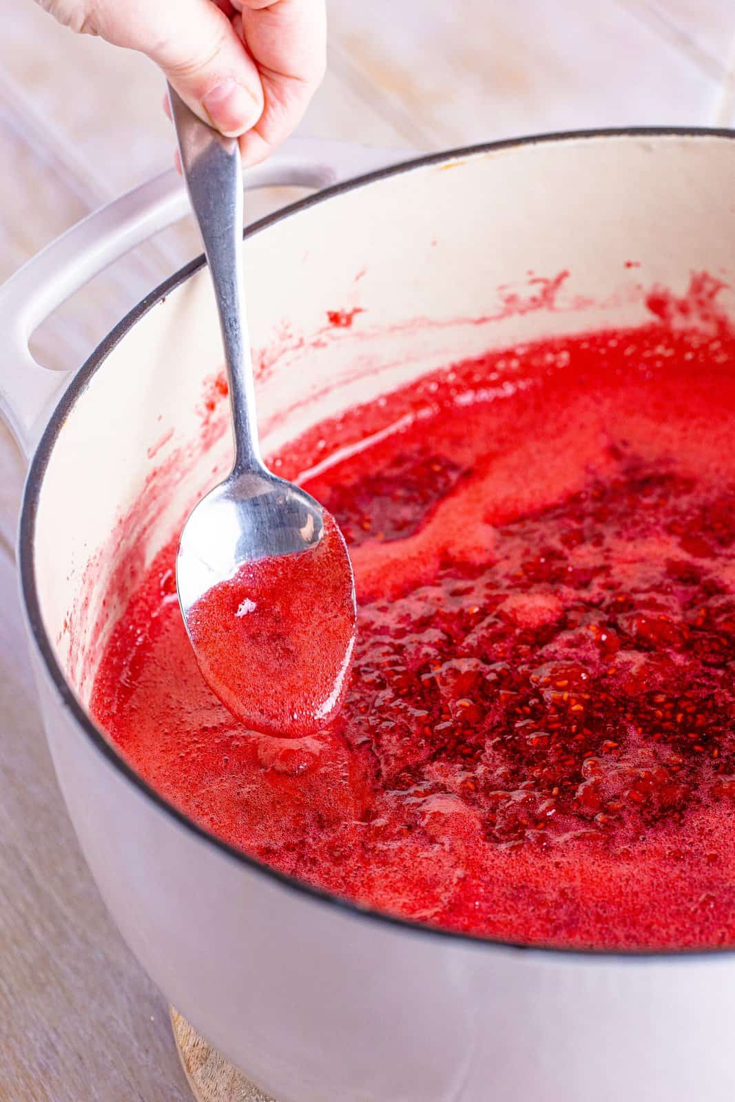 A spoon holding some jam mixture over a pot.