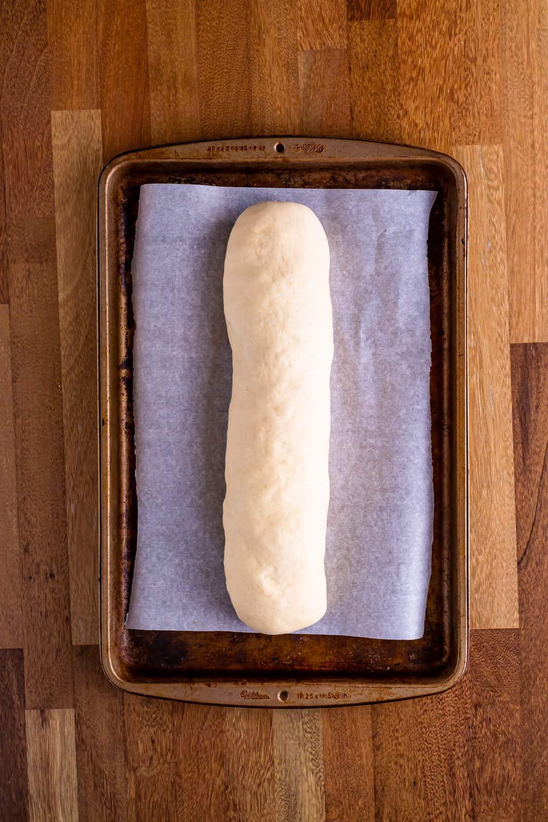 A parchment lined baking sheet with an uncooked sausage bread loaf. 