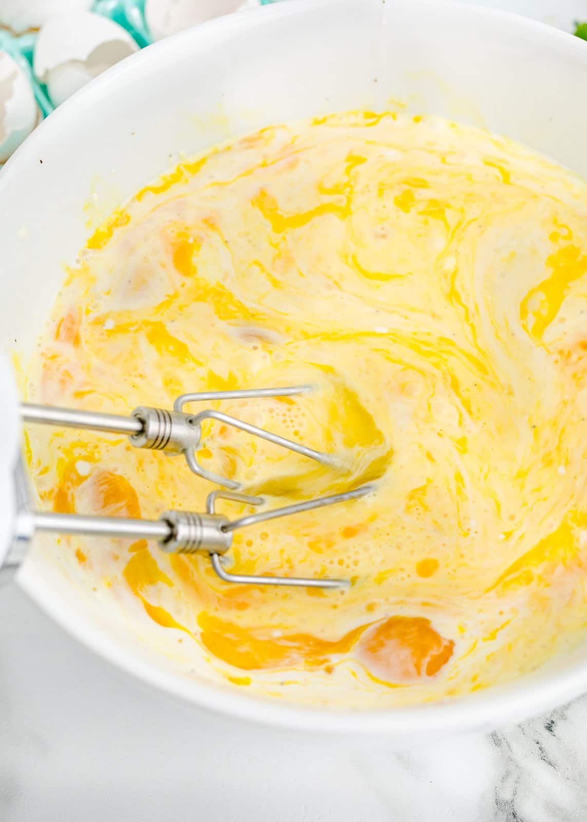A mixing bowl with beaters and eggs being mixed.