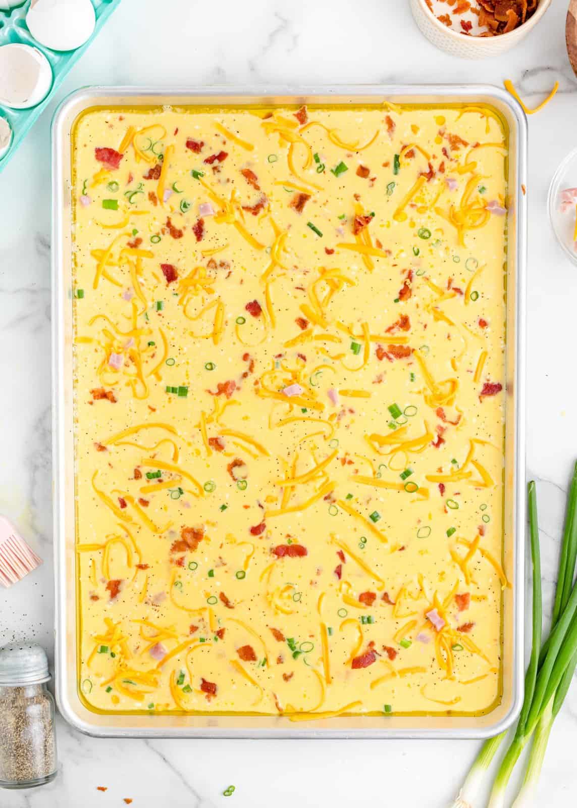 A sheet pan with eggs, bacon, scallions, and cheese.