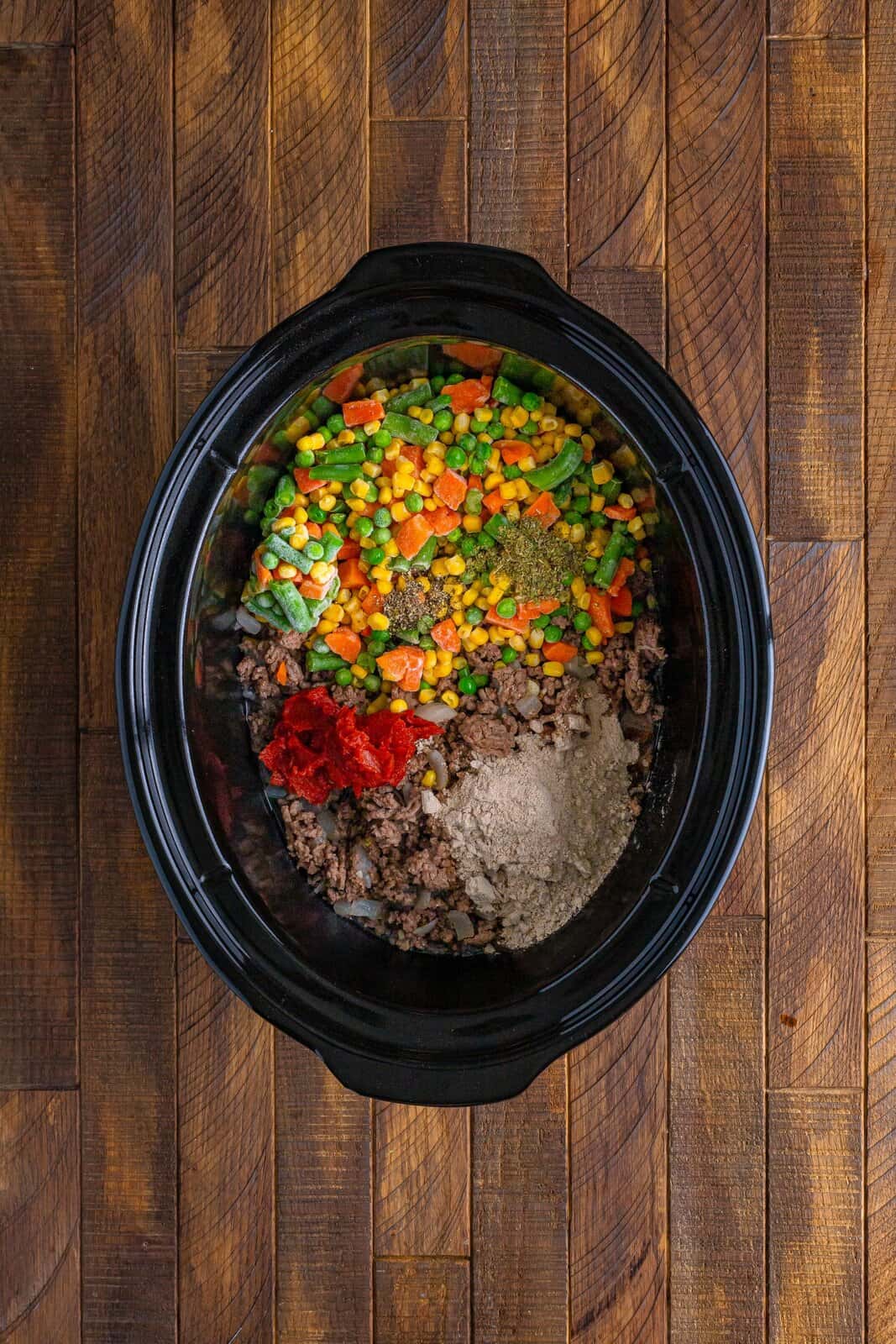 Slow Cooker with beef, frozen vegetables, tomato paste, water, gravy mix, and herbs and spices.