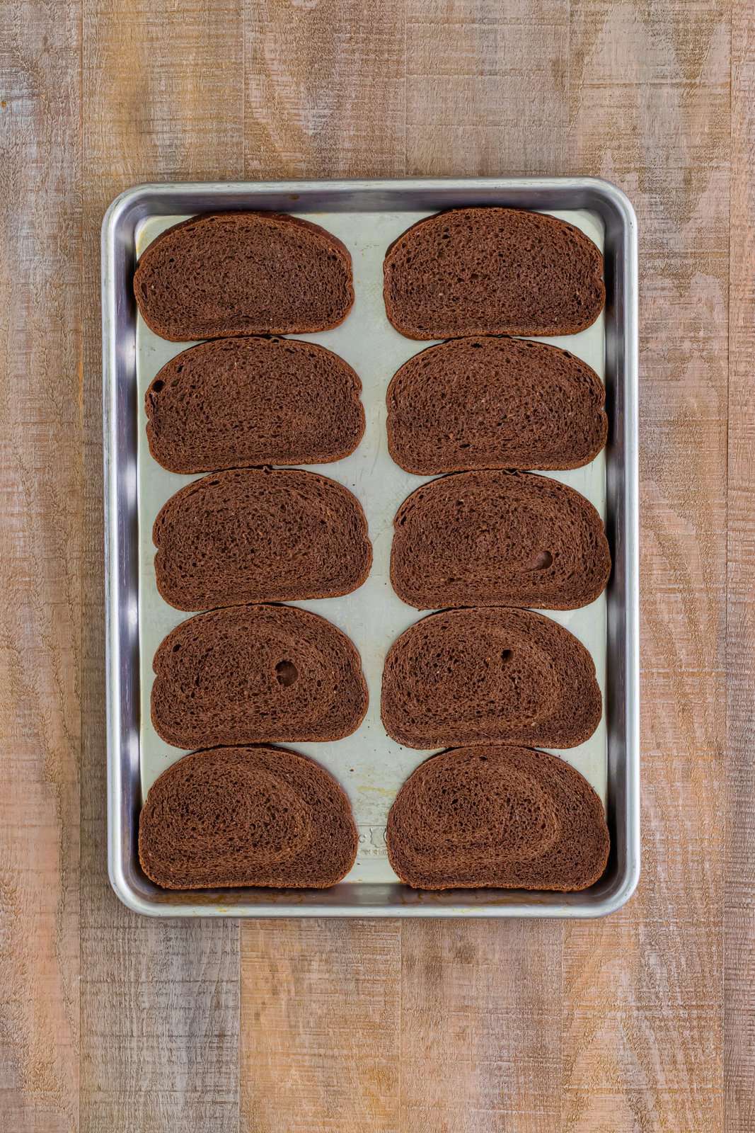 A baking sheet with ten pieces of pumpernickel bread.