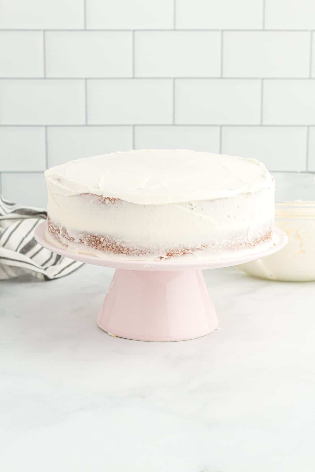 A homemade white cake with a crumb coat of frosting.
