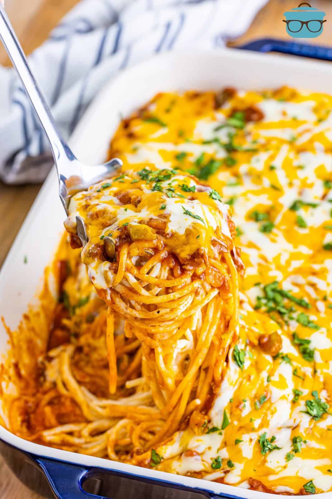 A baking dish full of Mexican million dollar spaghetti with a serving dish taking a serving out.