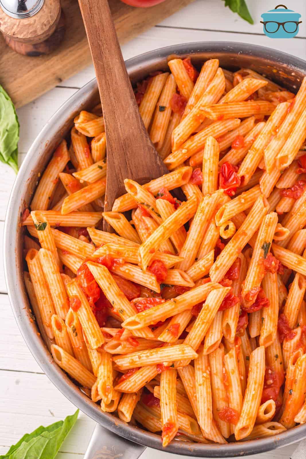 A pot of Penne Pasta with Tomato sauce and a wooden spoon being dipped in it.