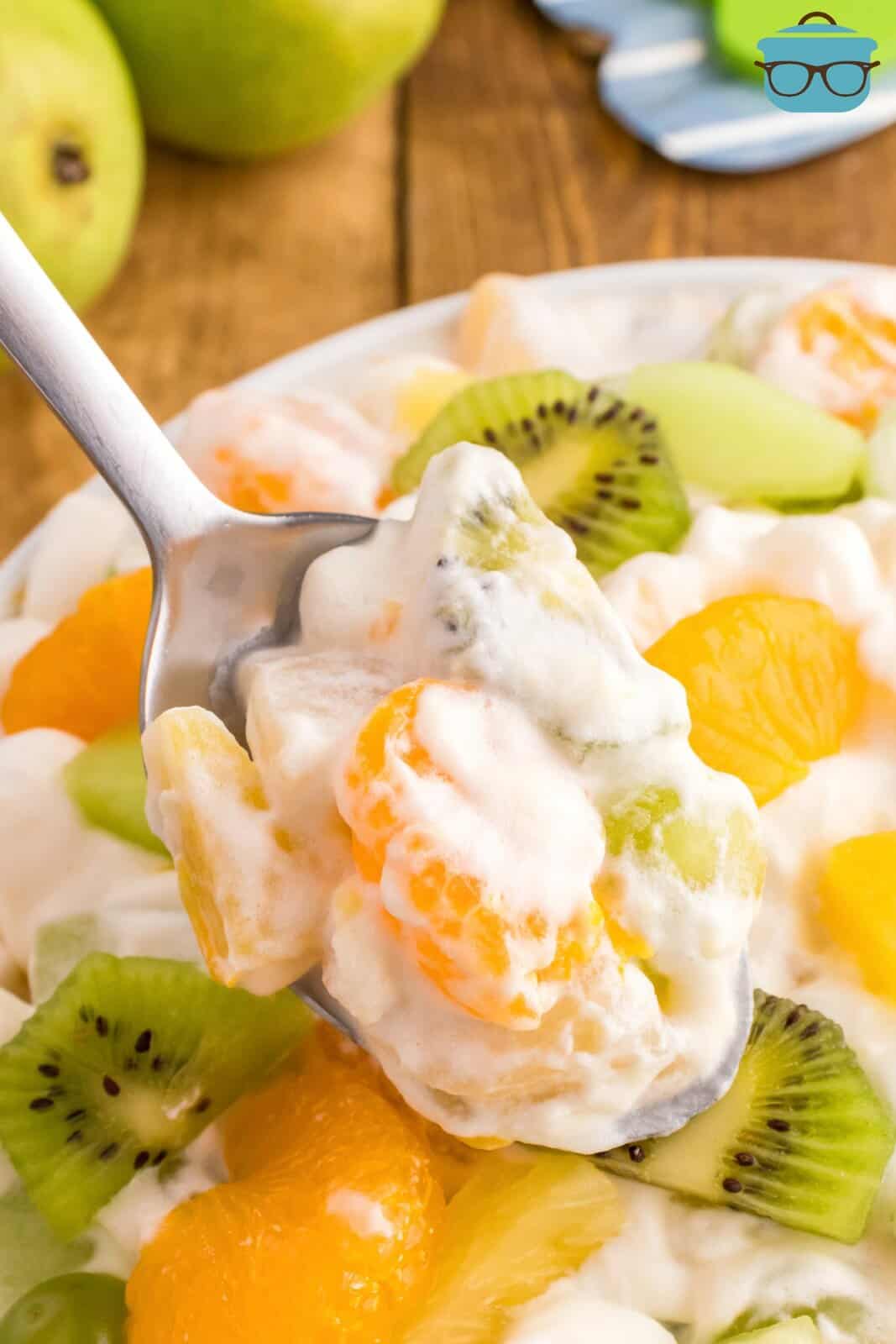 A spoon holding. a bite of ambrosia salad over a bowl.