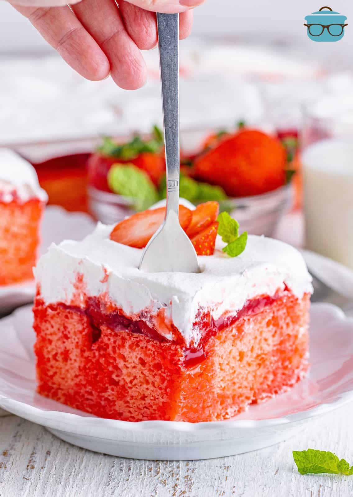 A fork standing in a slice of strawberry poke cake.