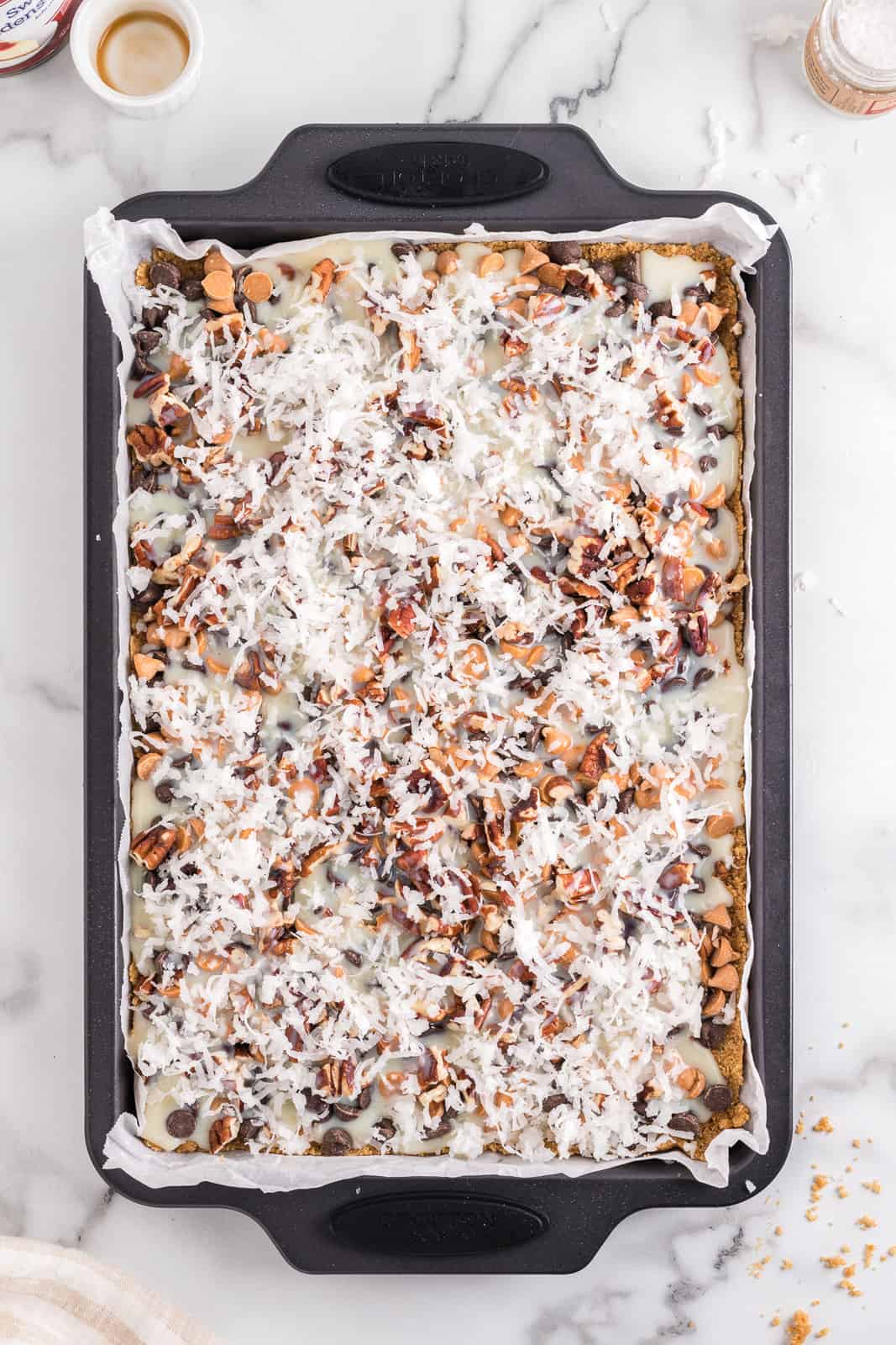 Baking chips, nuts, vanilla, condensed milk and shredded coconut on a crust.