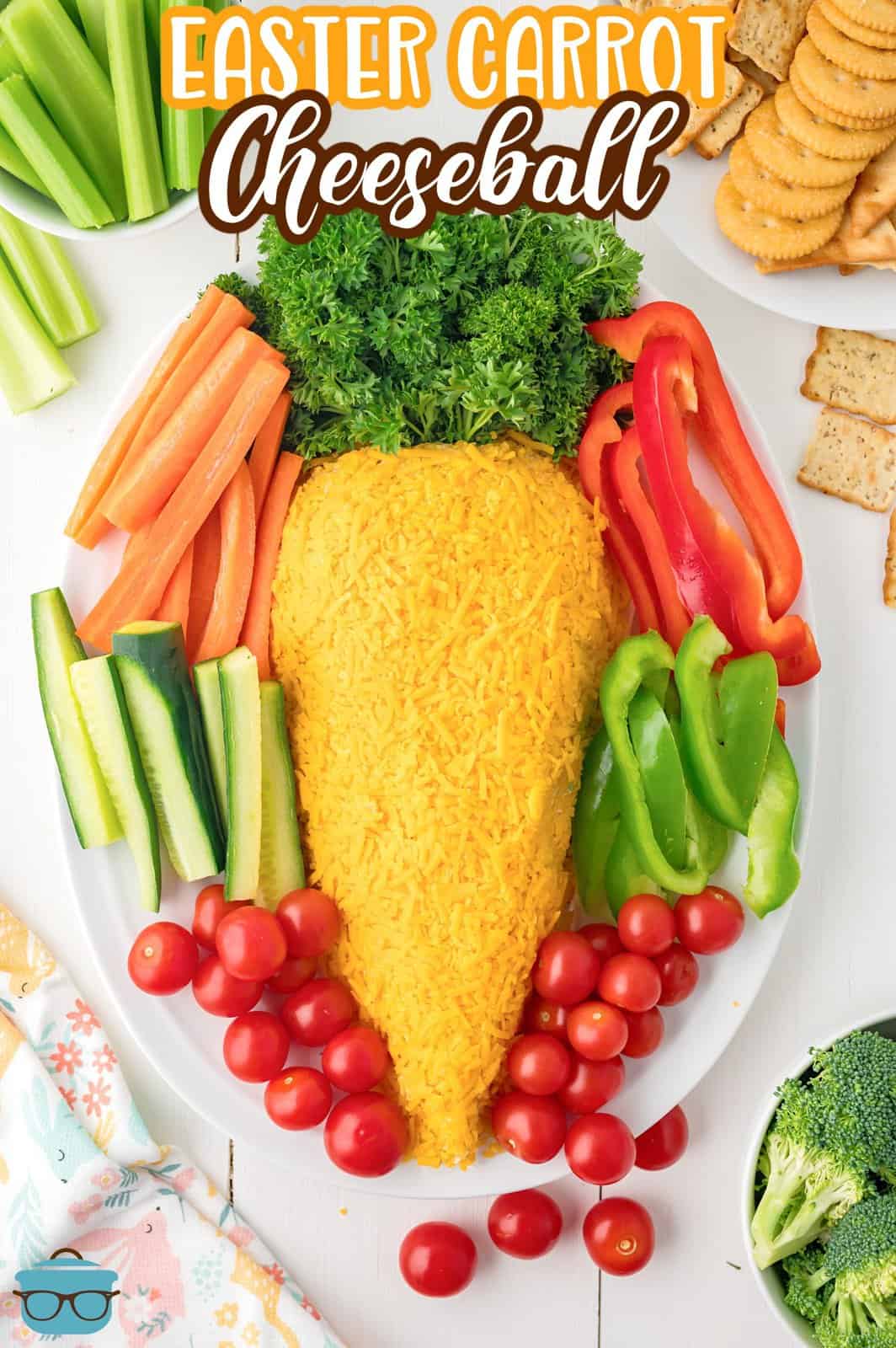This is a photo of an Easter Carrot Cheeseball on a white plate with vegetables - tomatoes, peppers, broccoli, cucumber and carrot. 