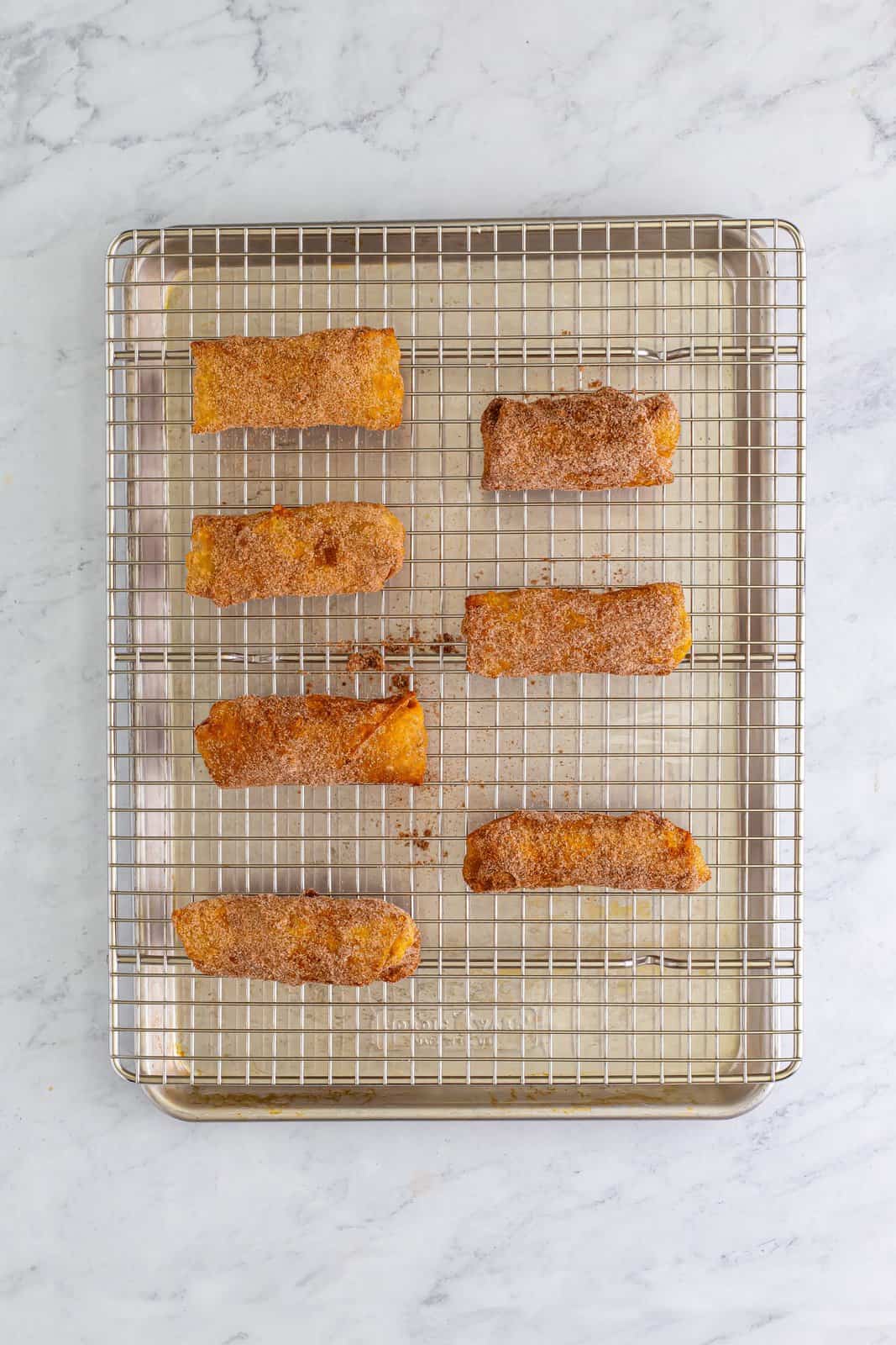 Cinnamon sugar coated apple pie egg rolls on a wire rack and baking sheet.
