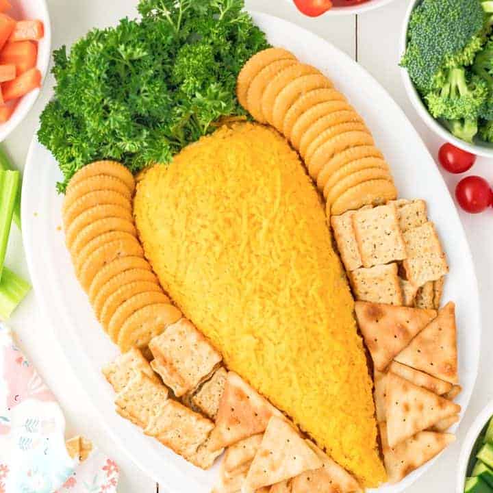 An Easter Carrot Cheeseball on a platter with crackers and other dippables around it.